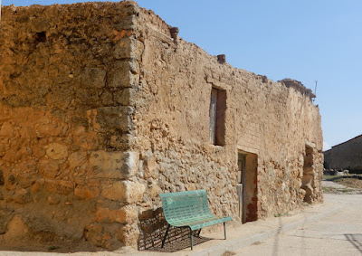 Construcción derruida de adobe y piedra con un banco verde apoyado allí