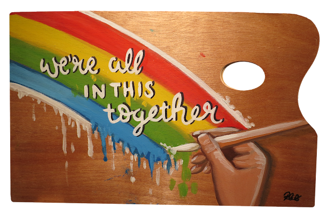 A wooden pallete painted with a hand painting a rainbow and the words 'we're all in this together'