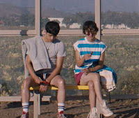 2 teenage boys sit at a bus stop