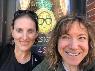 A selfie of Natalie and me, smiling, in front of the painting of a pineapple wearing sunglasses on a store sign.