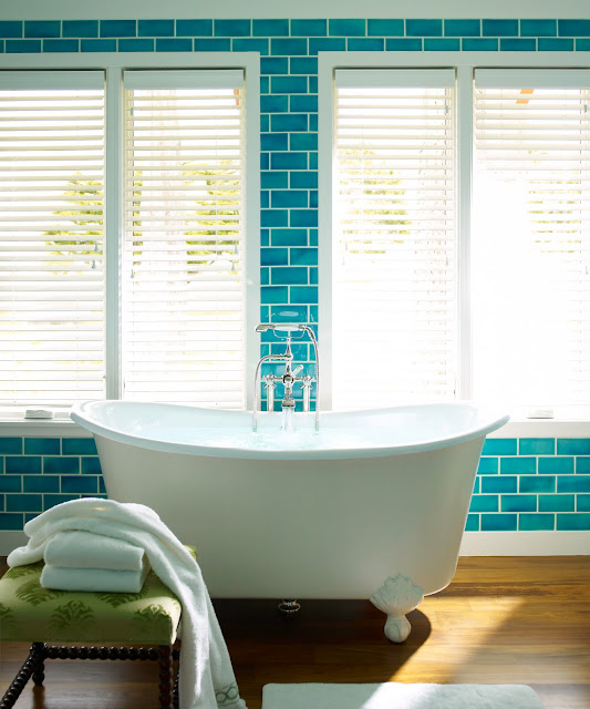 A traditional clawfoot tub pops against a wall of peacock blue floor to 