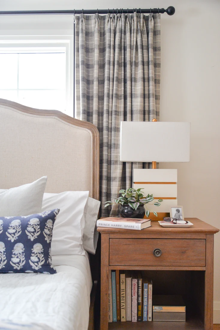 plaid bedroom curtains behind tall headboard and wood side table