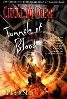 A teenage boy in baggy clothing walks thorough a large circular tunnel filled with blood and at least one skeleton.