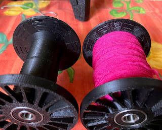 Two Falcon bobbins, side by side. The left one is empty and the right one is about one third full of fine, hot pink singles.