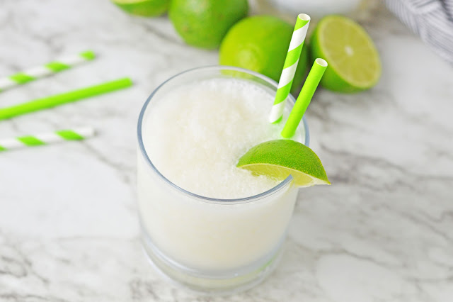 slushie in a clear glass with lime garnish and paper straws.