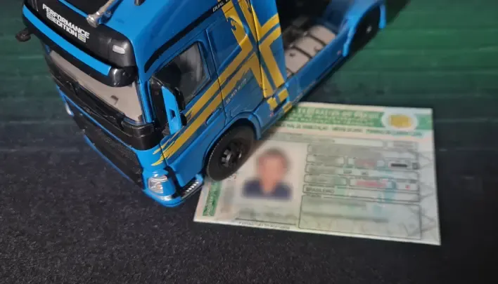Foto com um caminhao de brinquedo na cor azul encima de uma carteira de motorista