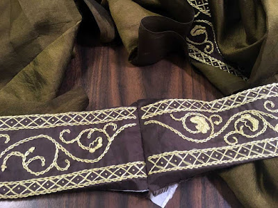 Two ends of gold embroidery on brown silk, seamed together and with crumpled green-gold silk around them.