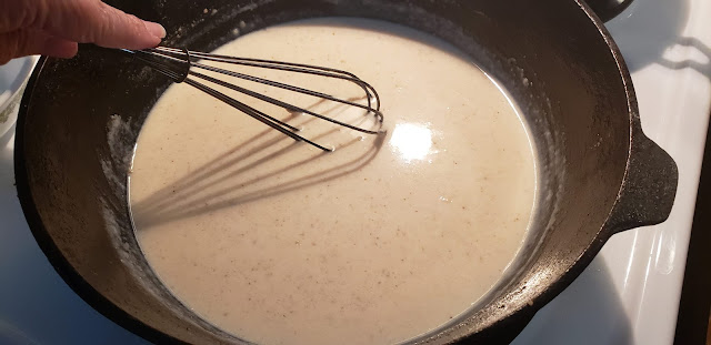 Black iron skillet whisking white gravy.