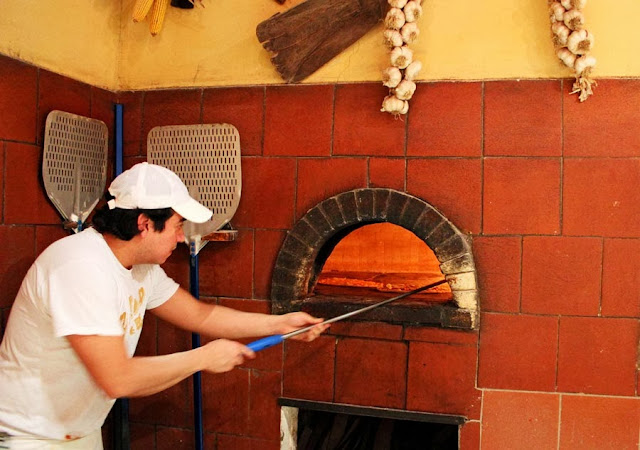 pizza being placed in wood fired brick oven