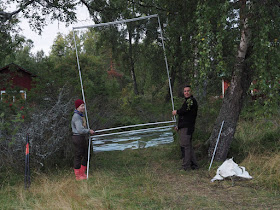 Kaksi ihmistä asettelee suorakaiteen muotoista pyydystä. 