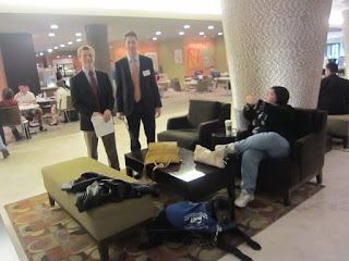 Michele and Coach are sitting in the lobby area as two of our students stand and look on (Max and Jake).