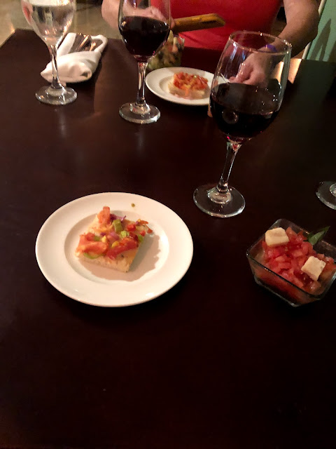 A table with 2 glasses of red wine, and 2 plates of bruschetta