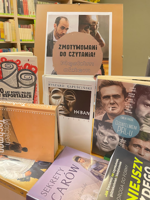 Na ladzie bibliotecznej znajduje się pionowy plakat "Zmotywowani do czytania: Męskim okiem" na małej sztaludze oraz kilka książek, które traktują o mężczyznach.