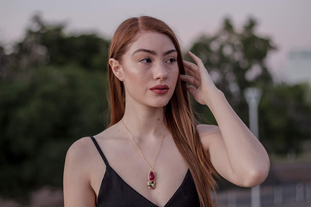 A long-haired woman wearing a purple and gold necklace.