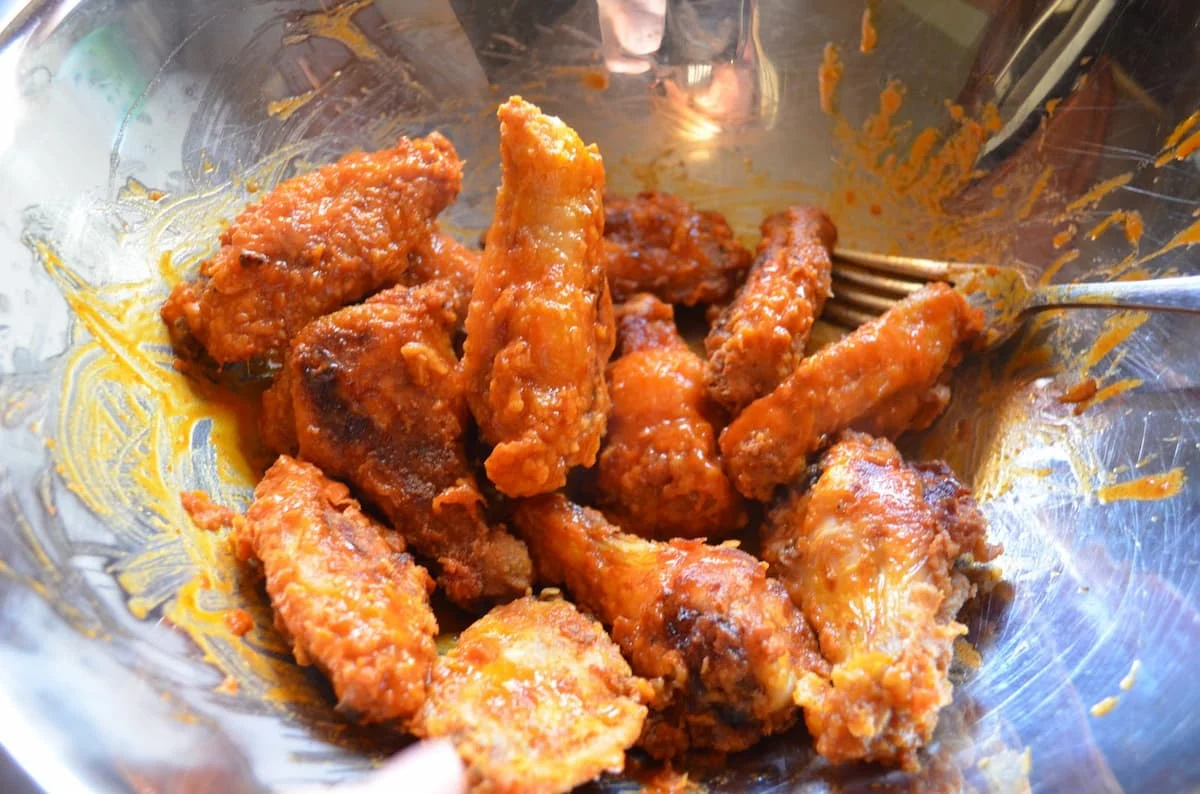 Fried Hot Wings tossed with hot sauce in a large stainless steel bowl.