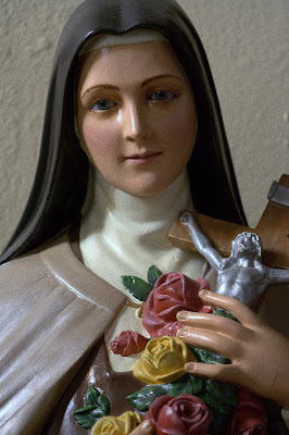 Statue of Saint Therese holding a crucifix and roses.