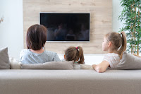 Madre y dos niñas frente a la televisión apagada, donde ven su reflejo.
