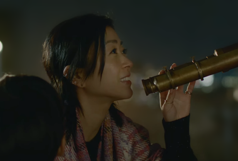A screenshot of Hikaru Utada from an Itochu TV commercial. The shot features Hikaru with a telescope, as their son is stood beside them.