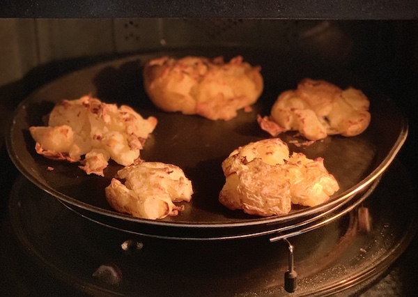 Golden baked, gently crushed potatoes in an oven tray still in the oven.