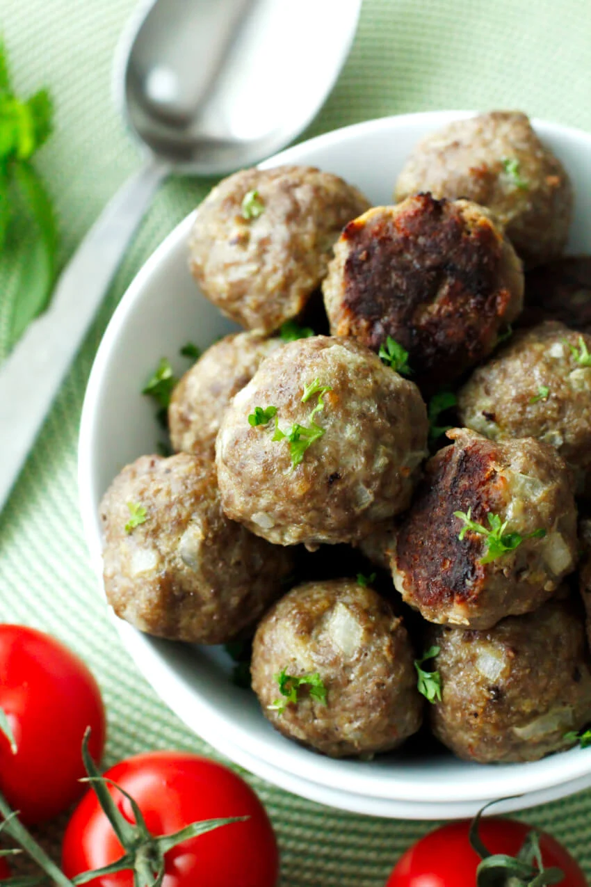 Oven Baked Mini Meatballs in a white bowl with a spoon and fresh tomatoes next to the bowl.