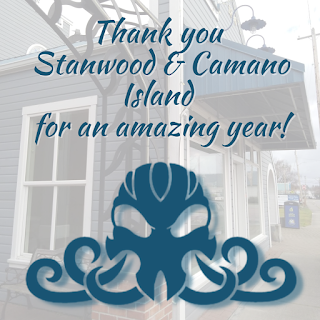 Image:  semi-translucent photograph of the side of a building.  Blue text and the shop Cthulhu logo are in the front.  Blue text reads: Thank you Stanwood & Camano Island for an amazing first year!