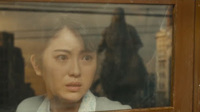 Noriko (Minami Hamabe) looks in horror as Godzilla approaches her train. Godzilla is reflected in the window.