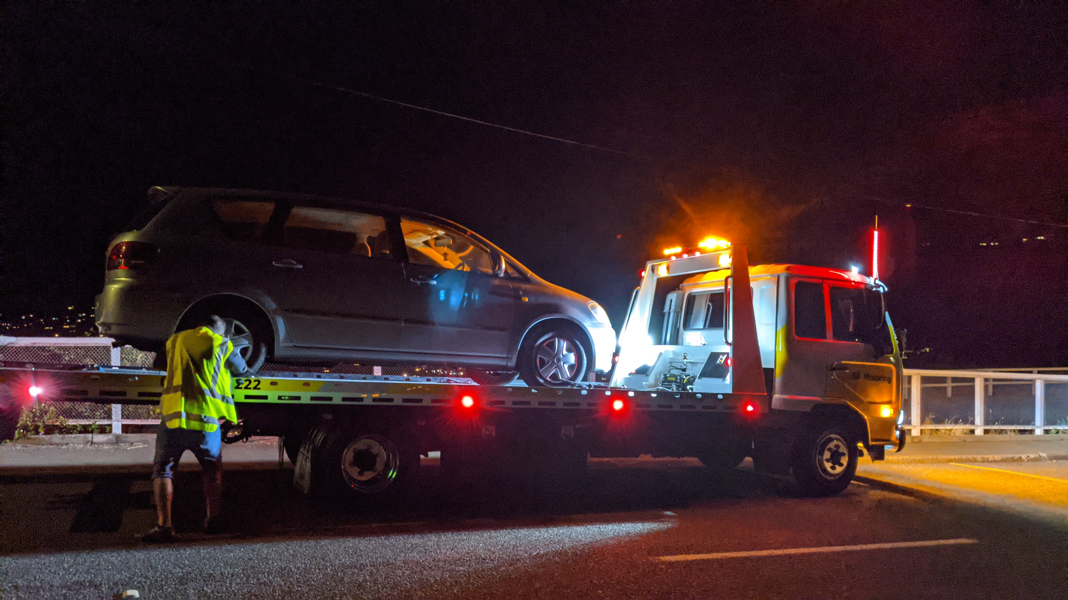 Broken car on the back of an AA service truck at night