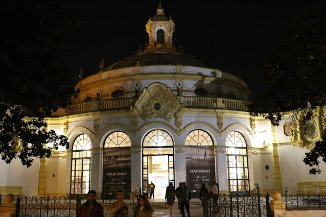 Entrada principal del Casino de Exposición de Sevilla iluminada por la noche con gente saliendo y entrando.