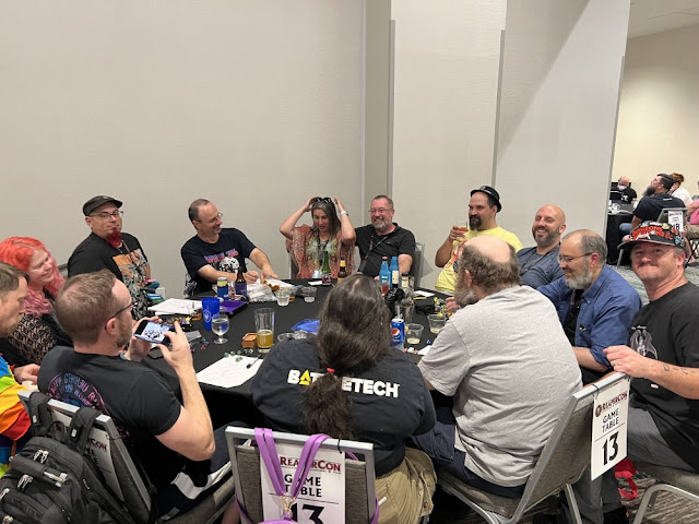 Photo of my gaming table at Reapercon. All seats are full, and extra seats have been pulled up. Everyone is laughing or smiling.