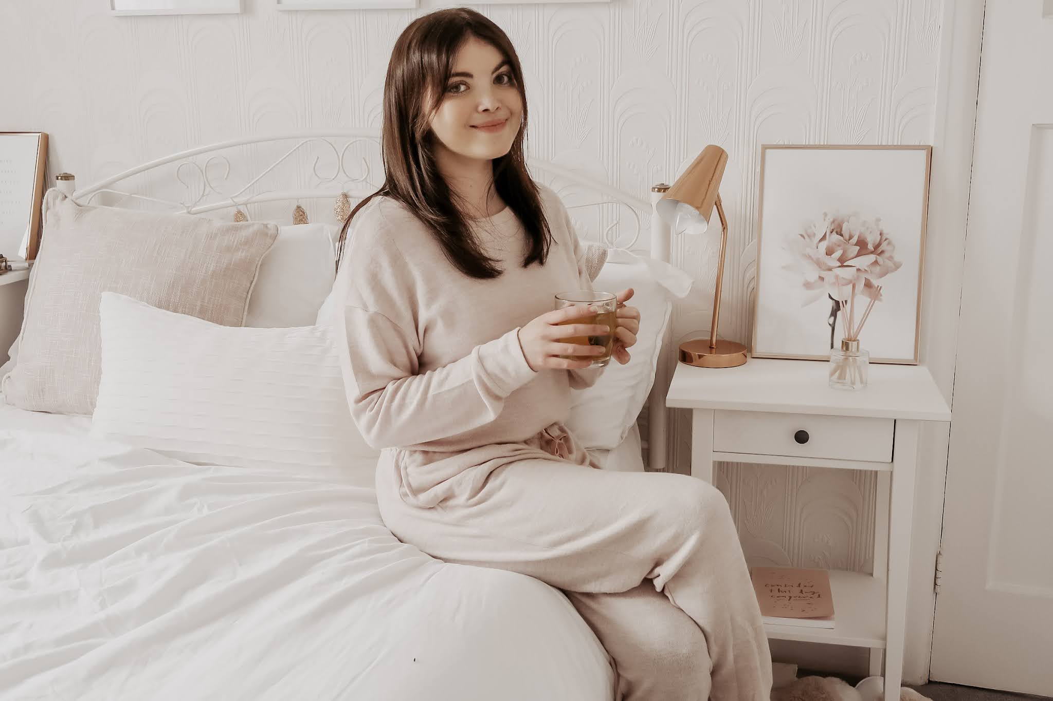 A woman sat on a bed holding a cup of tea.