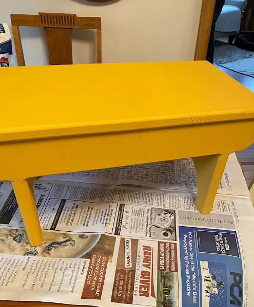 Photo of a wooden farmhouse bench being painted in Colonel Mustard Dixie Belle Paint.