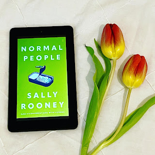 Kindle Fire with cover of Normal People by Sally Rooney and some tulips to the right