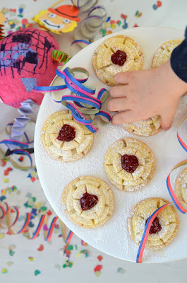 Fertig gebackene Rosenkrapfen aus dem Ofen – eine Kinderhand nimmt einen Krapfen vom Teller.