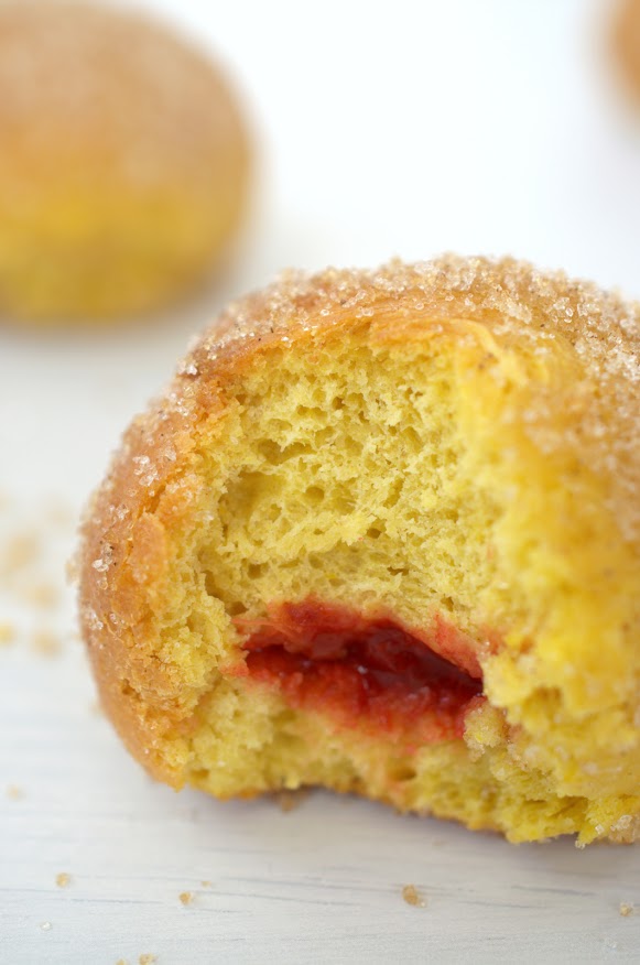 Flaumige Krapfen mit orangefarbenem Teig, roter Füllung und in Kristallzucker gewälzt.