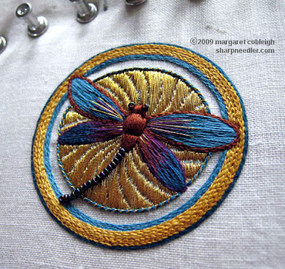 Completed embroidered dragonfly on top of underside couching in gold. This version of the dragonfly is in browns and blues with beads along the tail and touches of gold on the wings.