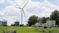 A wind turbine stands over a farmhouse in Adair, Iowa. (Credit: Charlie Neibergall/AP) Click to Enlarge.