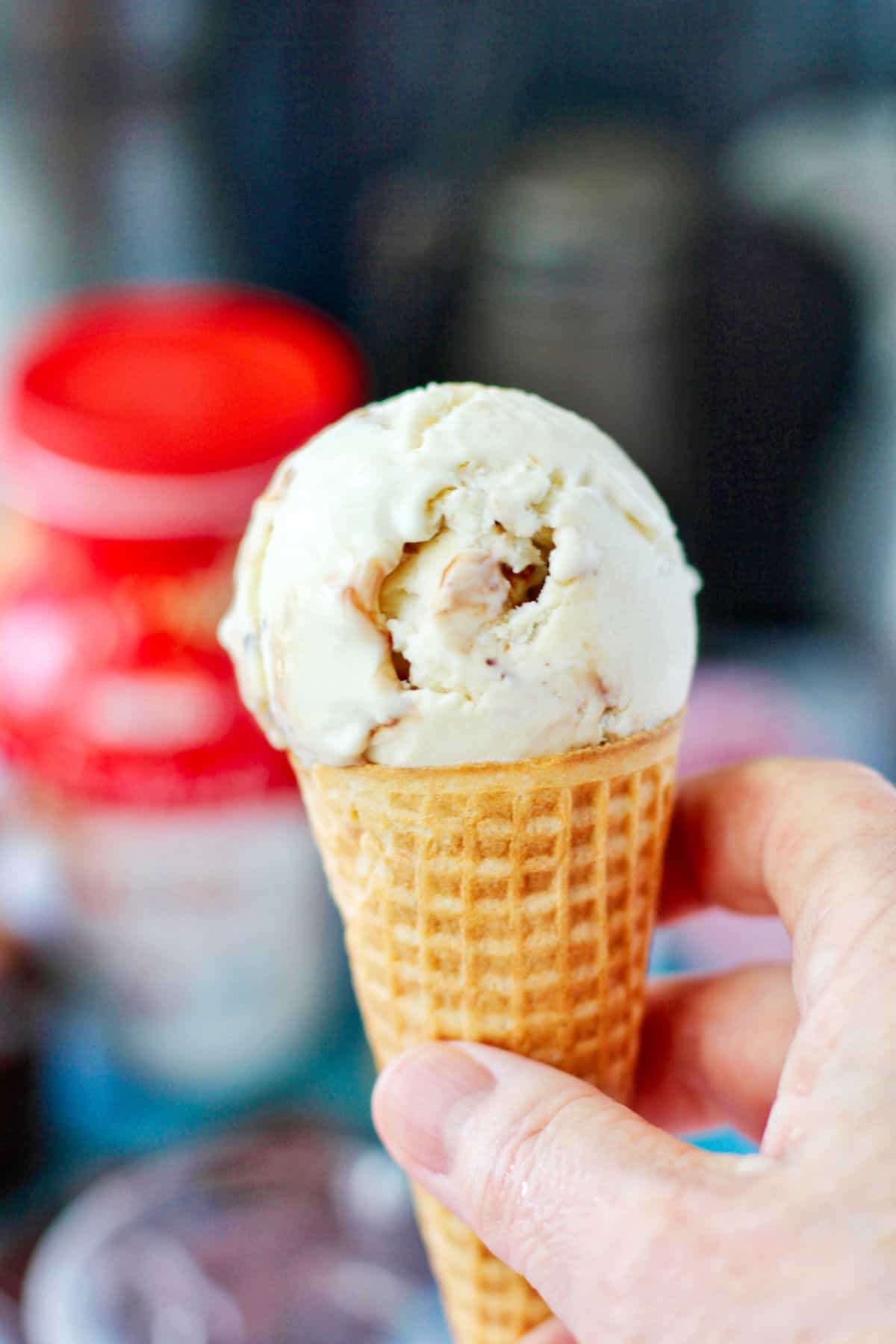 No Churn Tahini Ice Cream scoop in a cone held by a hand.