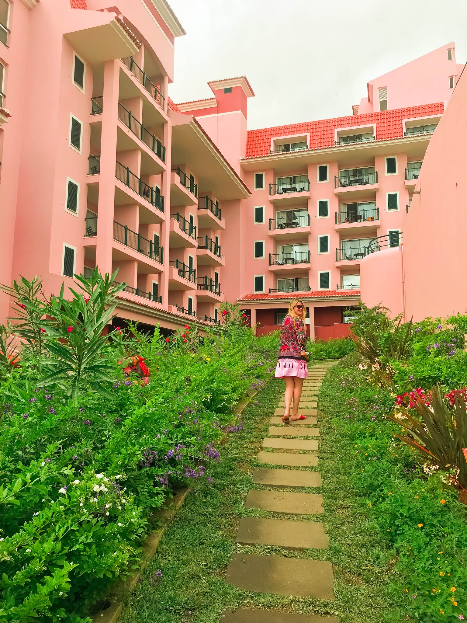 blonde-girl-in-pink-dress-and-floral-kimono-smiling-and- walking-through-flowers-in-maderia