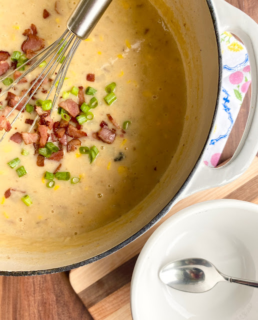 Dutch oven pot of cheesy potato soup topped with crumbled bacon and green onions.