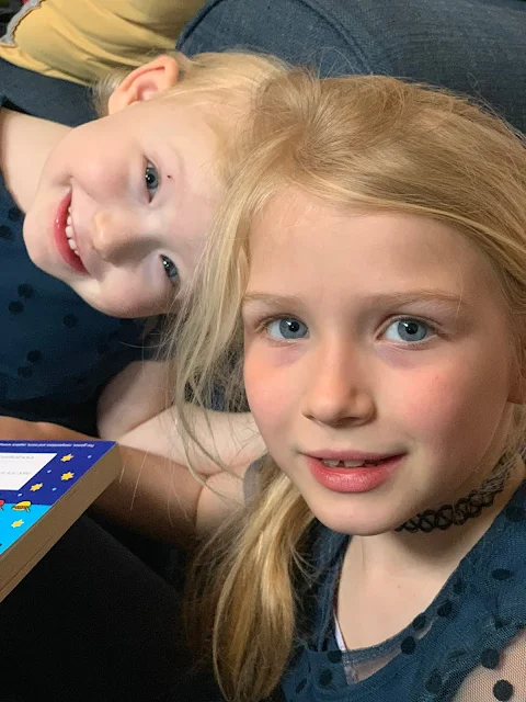 Blonde sisters aged 3 and 7 smiling at the camera in matching dresses