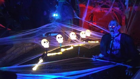 Nighttime photo. A front yard with fake spider web, five illuminated plastic skulls and an illuminated Frankenstein's monster.