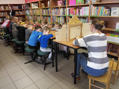 Na zdjęciu bibliotekarz czytajacy dzieciom opowiadanie za pomocą Teatrzyku Kamishibai