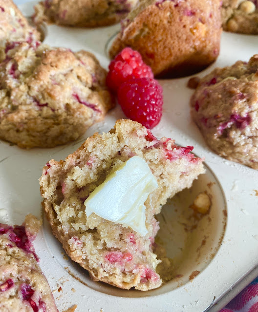 Split white chocolate raspberry muffin with butter sitting in a muffin tin.