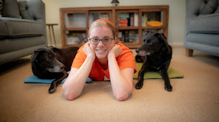 Dog trainer Jessica Ring lies on the floor with her two dogs, one on each side of her, facing the camera