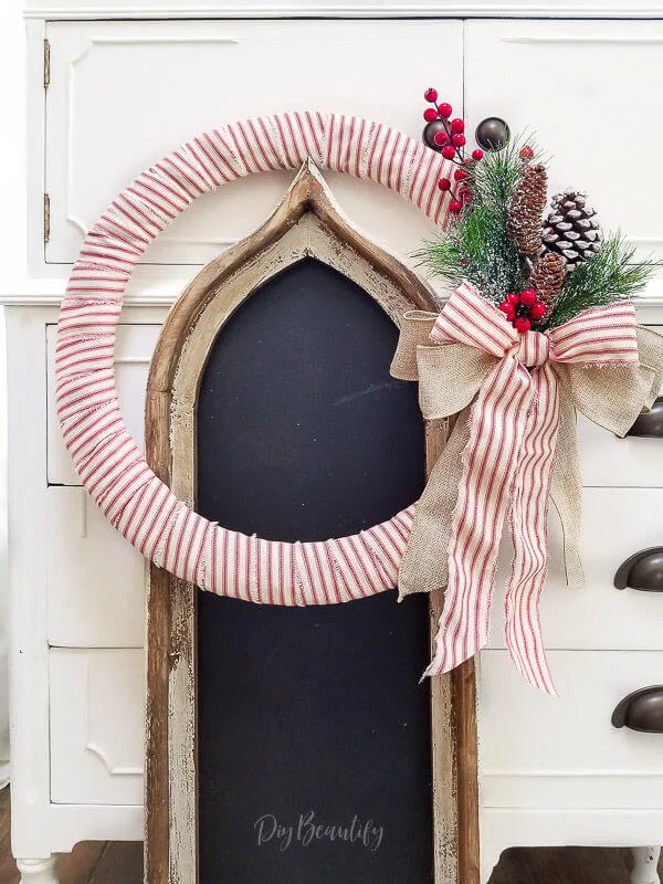 red ticking wreath leaning against white cottage dresser and chalkboard