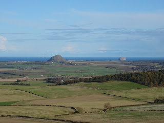 A view from the monument over green fields to a small but steep hill, Berwick Law and in the distance the dark rock of the Bass Rock.  Photo by Kevin Nosferatu for the Skulferatu Project.