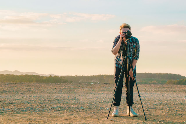 Fotográfo en un campo desierto enfocando su camara.