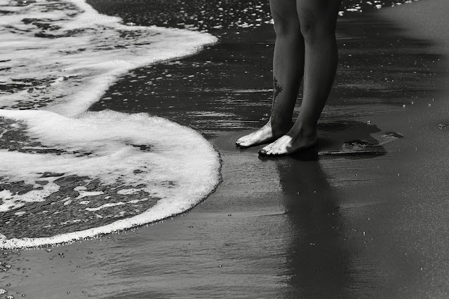 Barefoot on black sand beach with white sea foam