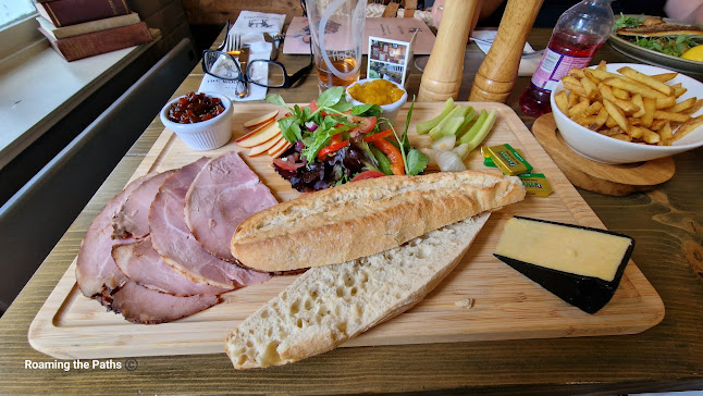 Lanscape shot of a Ploughmans Lunch from the Woolpack at Sopley. 4 slices of ham, a quarter of a small cheddar wheel, salad, pickle and picaclilli, salad, Pickled onions, warm half baguette on a wooded platter.