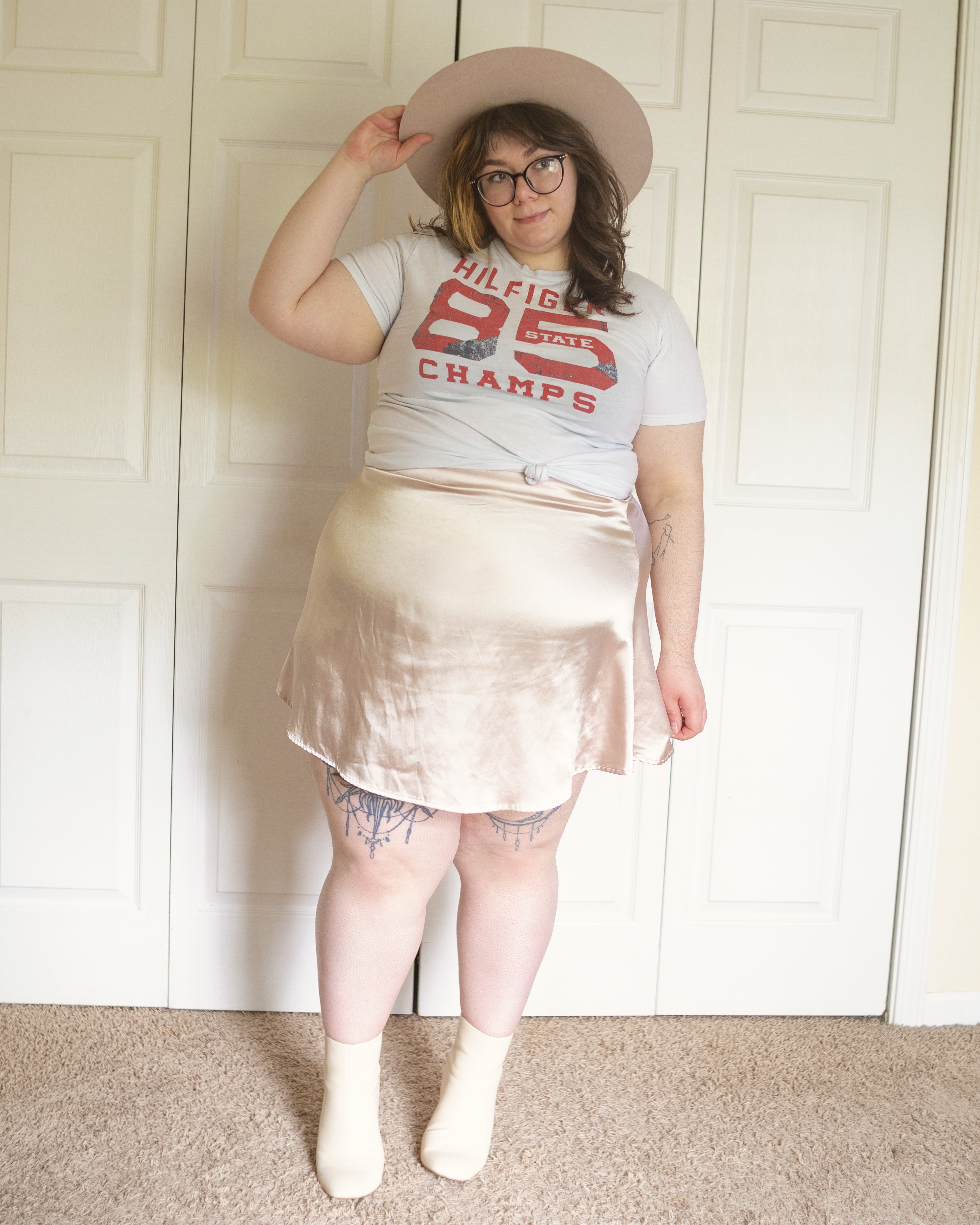 An outfit consisting of a white Tommy Hilfiger tee tied in the front and a pastel pink satin silk mini skirt and dusty pink, white square toe boots.